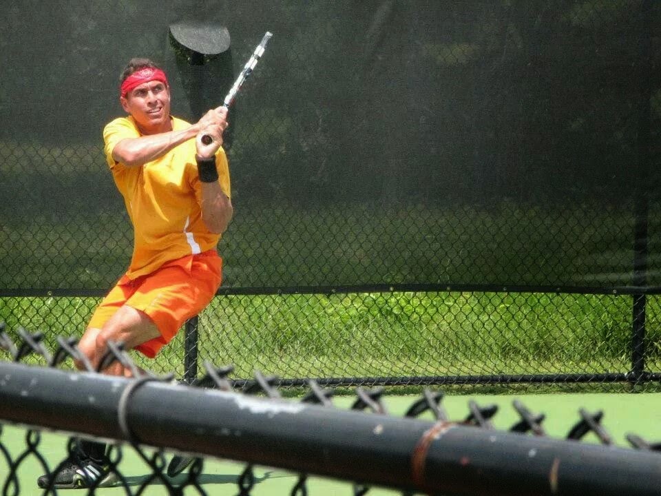 Aaron Krisan reaching for a backhand on an outdoor tennis court